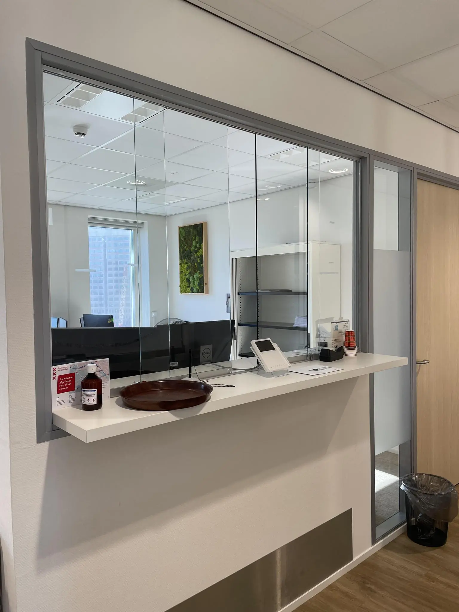 Balie van een kantoor op de Johan Cruijff Boulevard met een glazen scheidingswand en een receptie met desinfectiemiddel en informatiemateriaal.